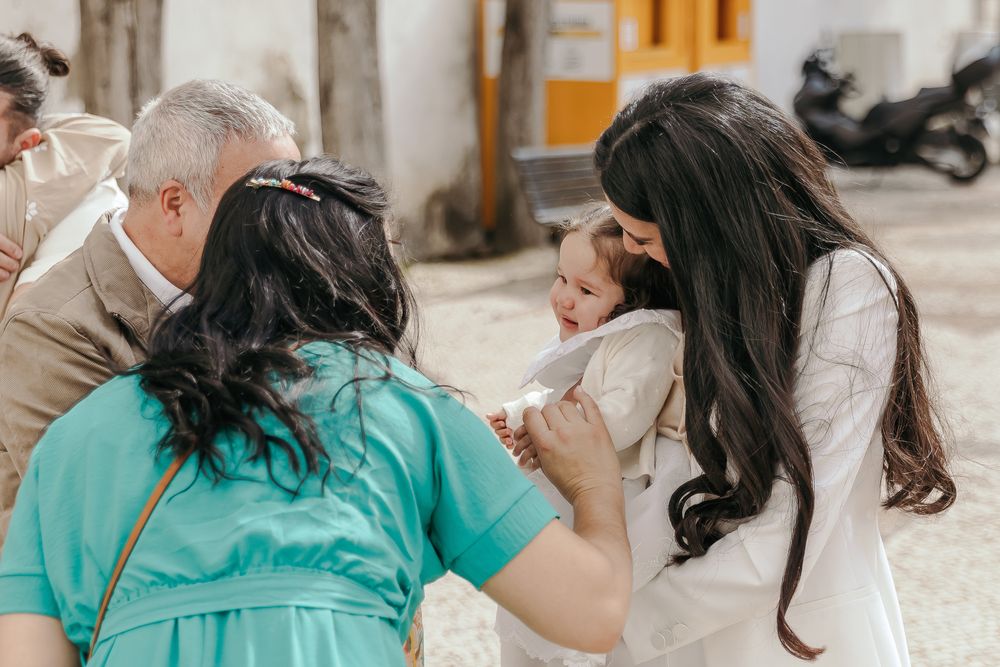 Family gathering outdoors as woman in white holds baby while others lean in to interact with the child.