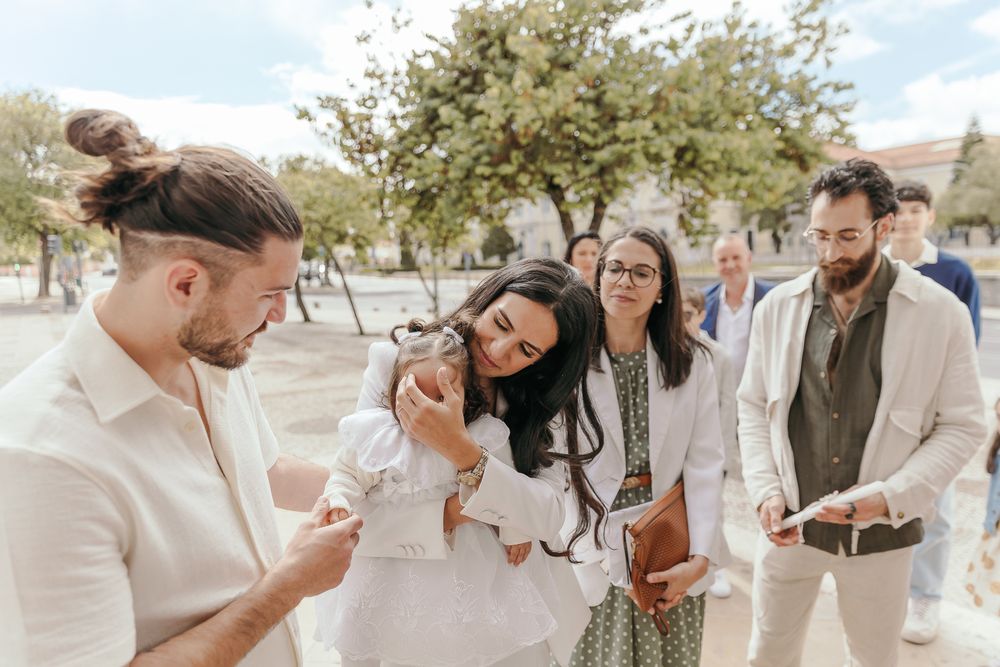 Group of young adults gathered outdoors, engaged in conversation, holding books and phones on a sunny day.