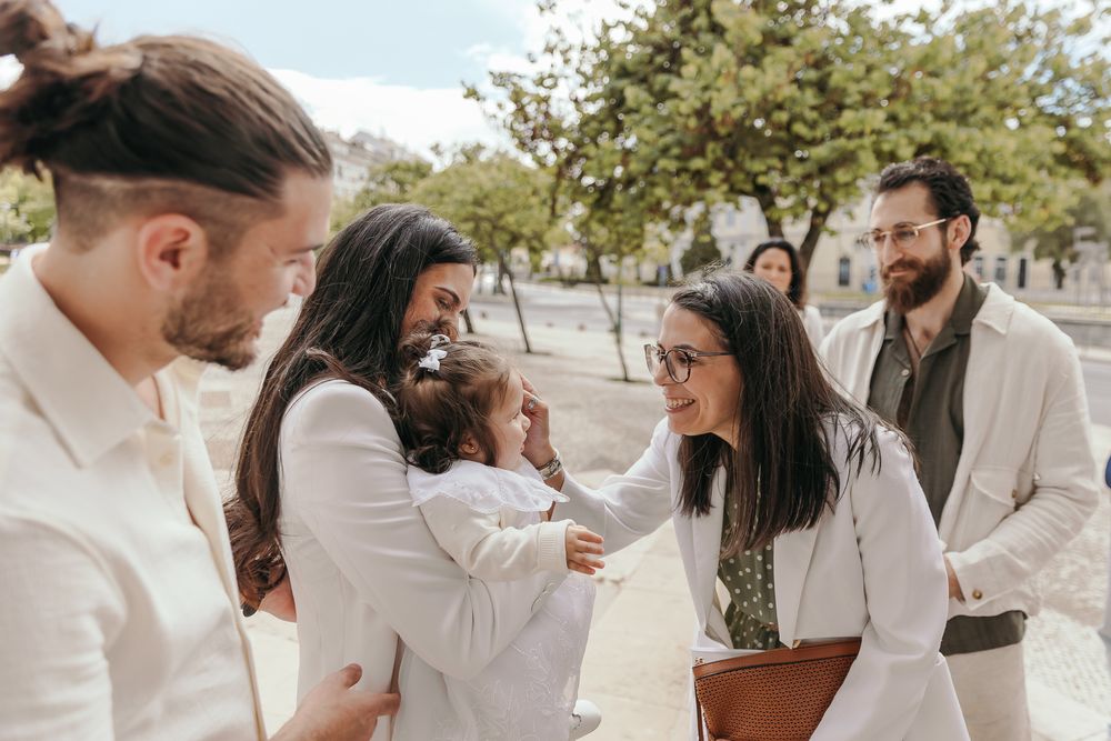 Group of friends in white outfits gathering outdoors, smiling and greeting a baby at a sunny social event.