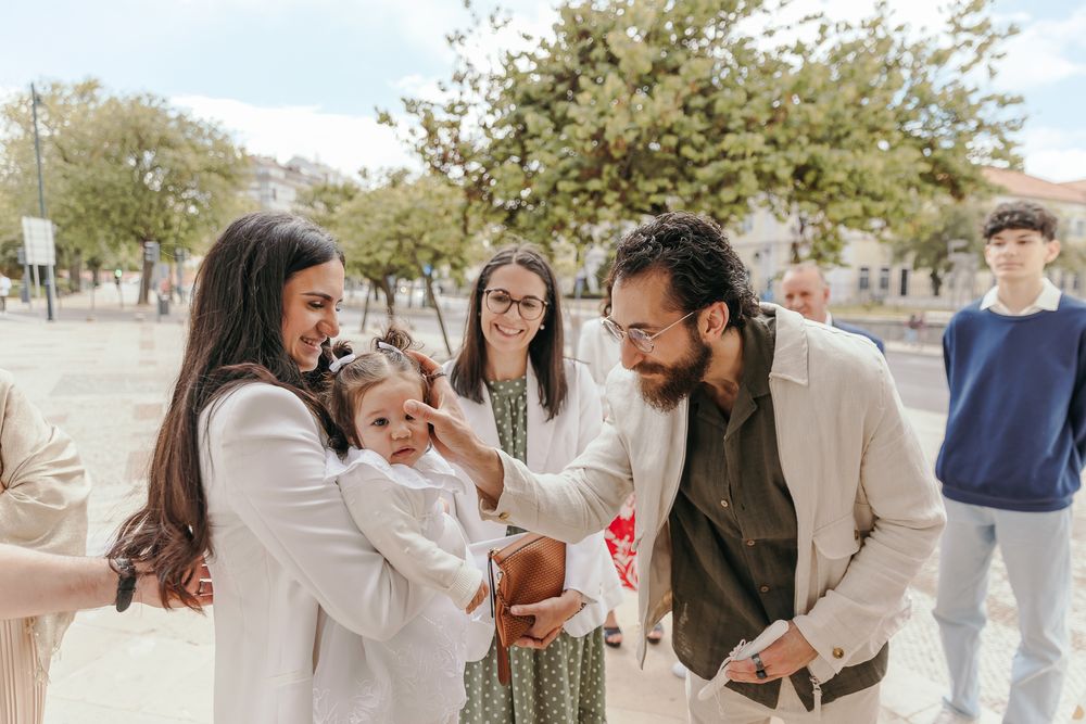 Family gathering outdoors as bearded man greets mother holding baby girl, with smiling guests in background.