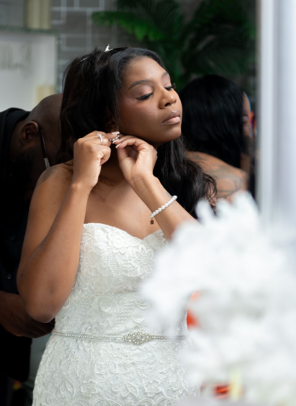The bride puts her earrings on in the mirror.