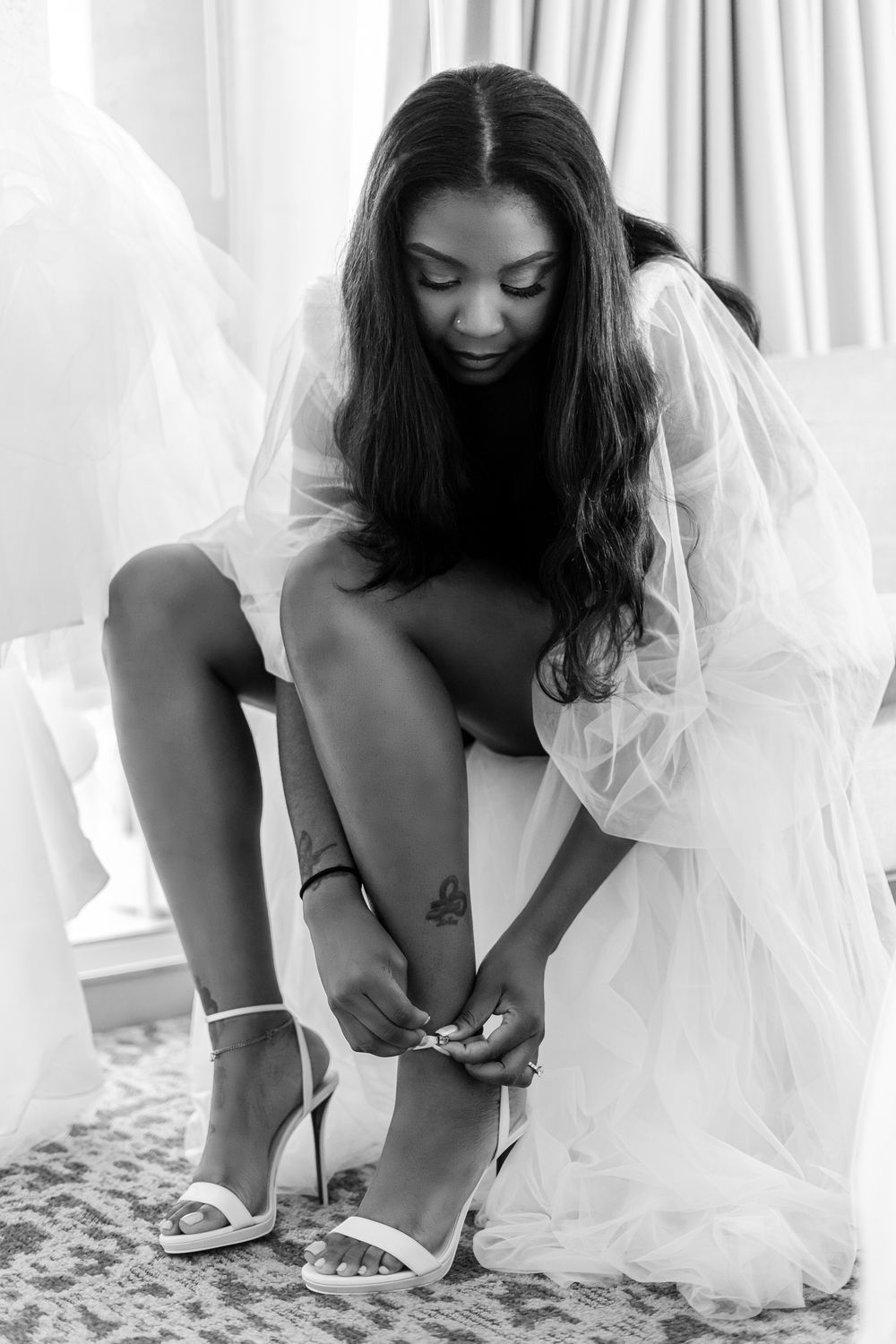 The bride puts the straps on her red bottom shoes while wearing her silk robe.