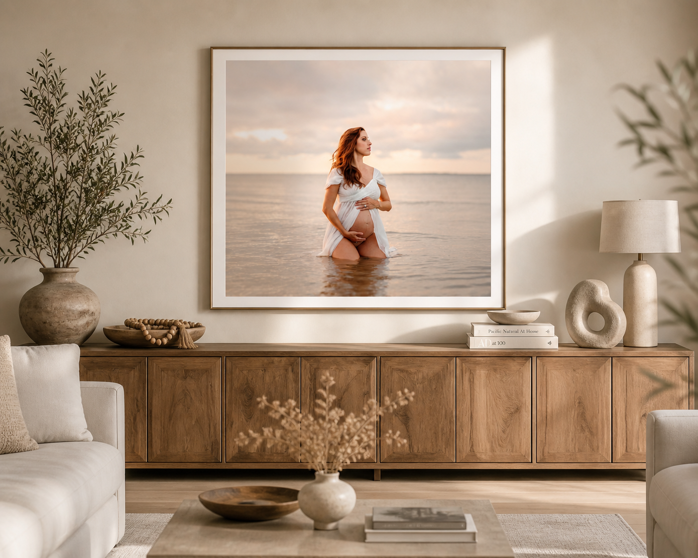A framed maternity photo of a woman standing in Hilton Head ocean water hangs above a wooden sideboard in a neutral coastal living room.