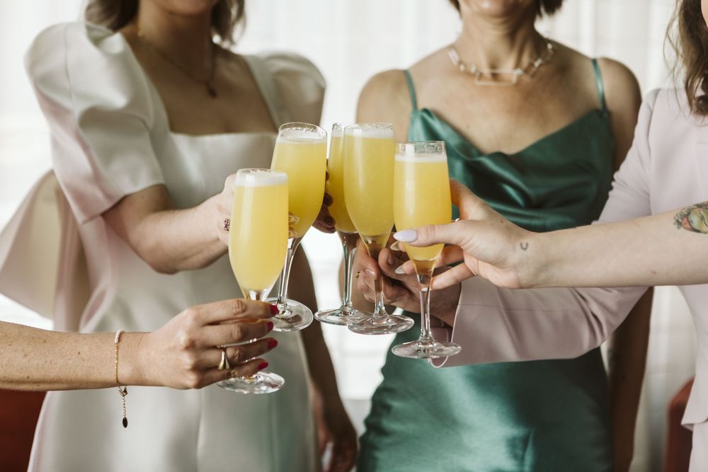 Women in elegant dresses toasting with mimosas at a bridal party celebration.
