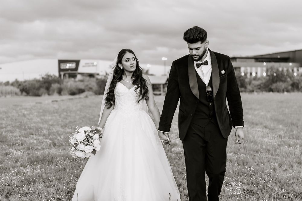 Bride and groom walking hand in hand in a field, black and white wedding portrait with bouquet.