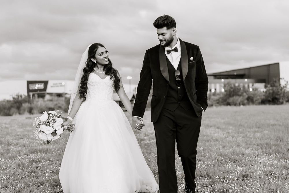 Black and white photo of bride and groom walking hand in hand across a grassy field on their wedding day.