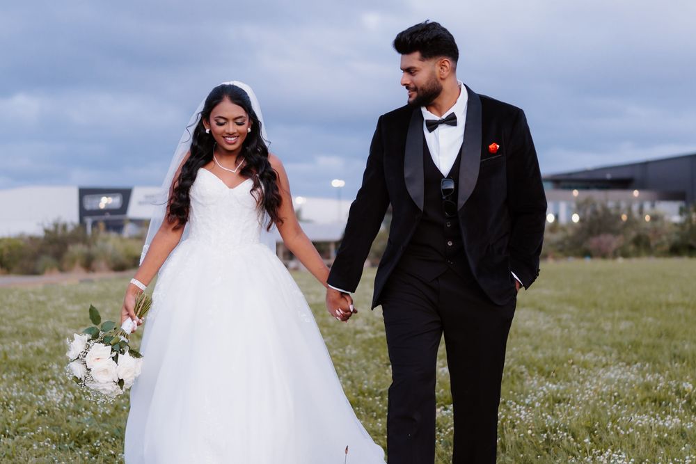 Smiling bride and groom holding hands walking through a green field on their wedding day.