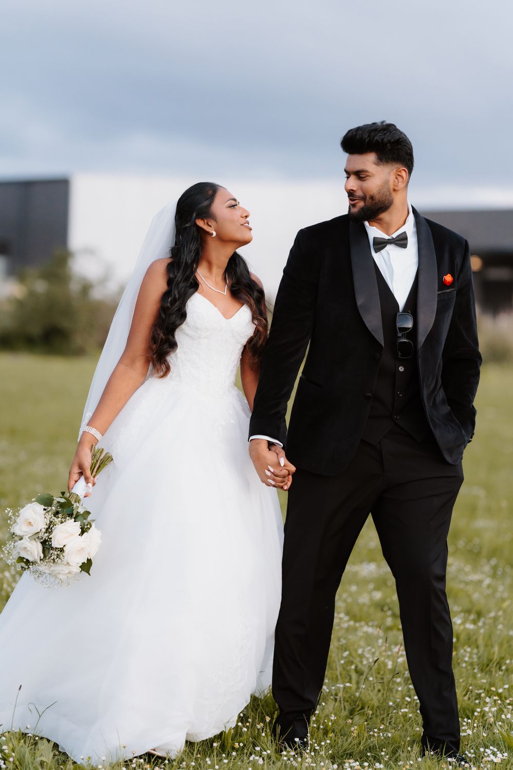 Wedding couple holding hands and gazing at each other in a green meadow at dusk.