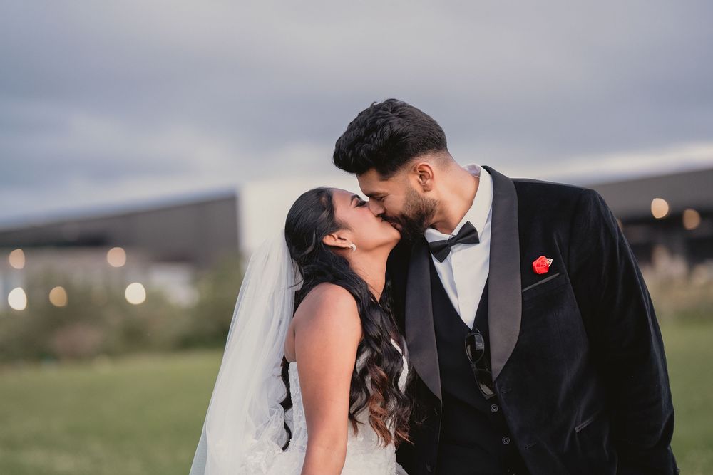 Bride and groom sharing a romantic kiss outdoors on their wedding day, groom in black tuxedo.