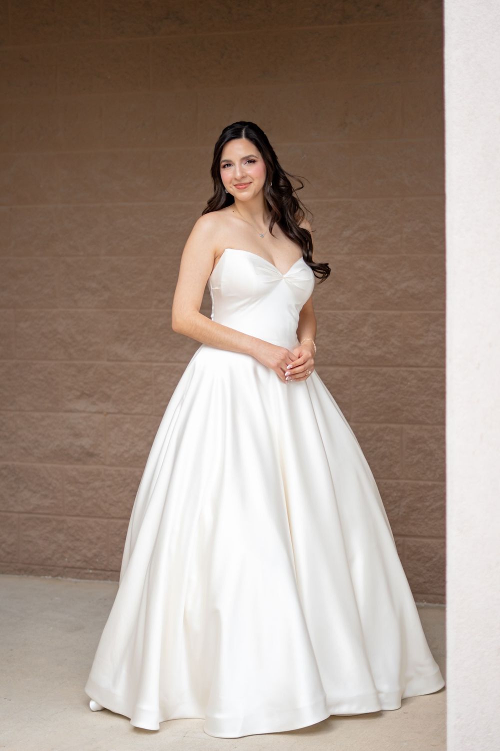 Elegant bride poses in a strapless white satin ballgown wedding dress with sweetheart neckline and full skirt.
