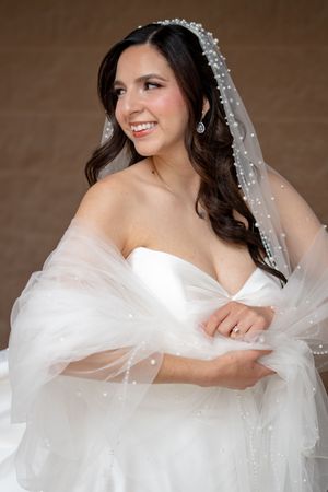 Radiant bride smiles in strapless white gown wearing a pearl-embellished veil and sparkling diamond earrings.