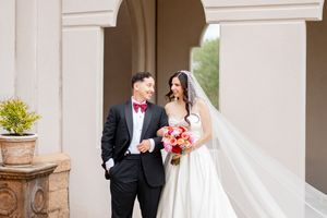 Happy couple in wedding attire walking outdoors, groom in black tux and bride in flowing white gown.