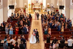 Aerial view of wedding ceremony in ornate church with guests filling pews and couple at altar.