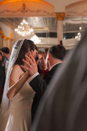 Bride in white veil and groom share an intimate moment covering their faces with hands during wedding ceremony.