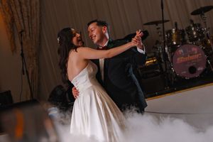 Bride and groom share their first dance on a fog-covered dance floor with a live band performing behind them.