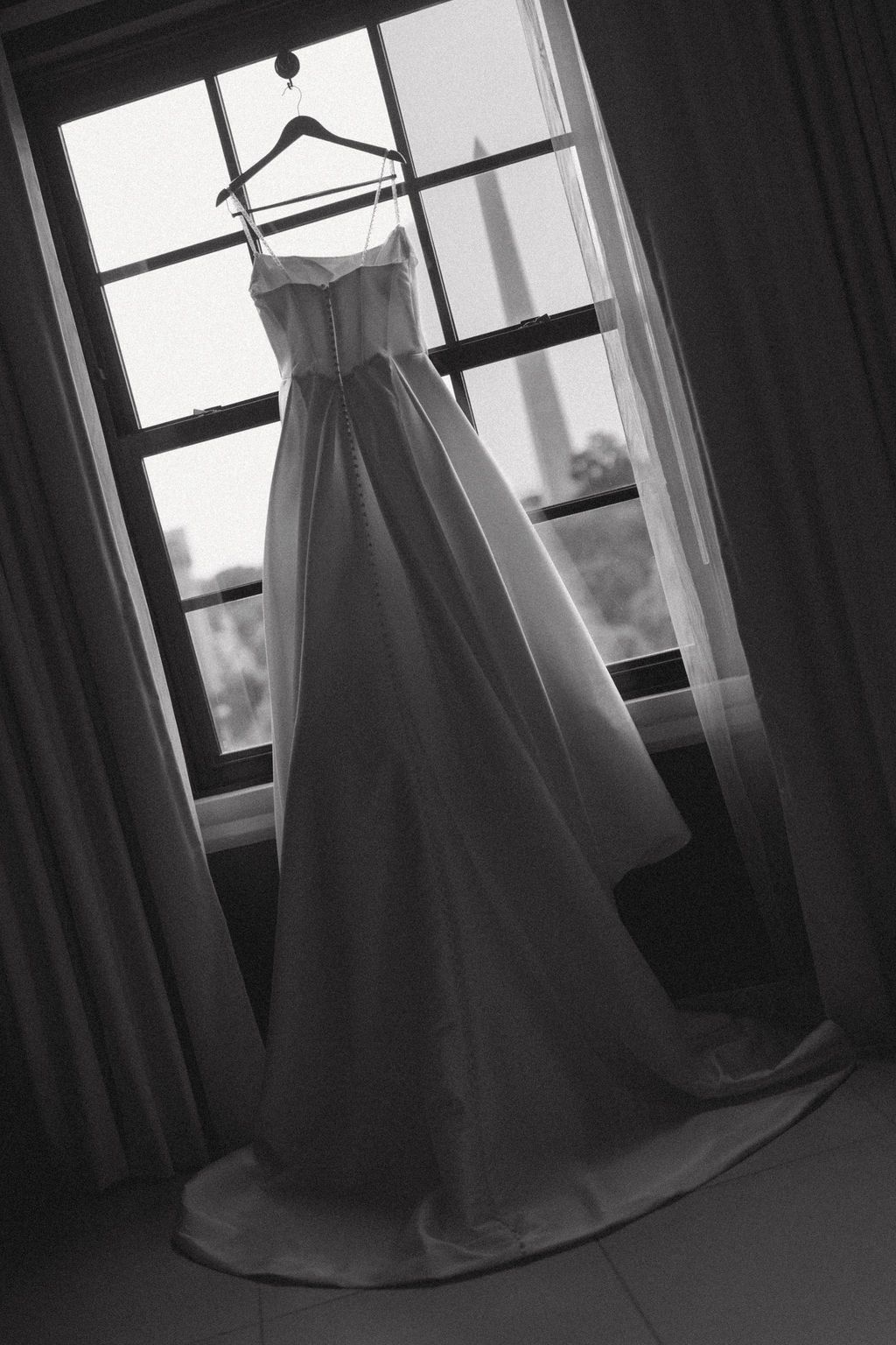 A wedding dress hanging in a window with the Washington Monument in the background