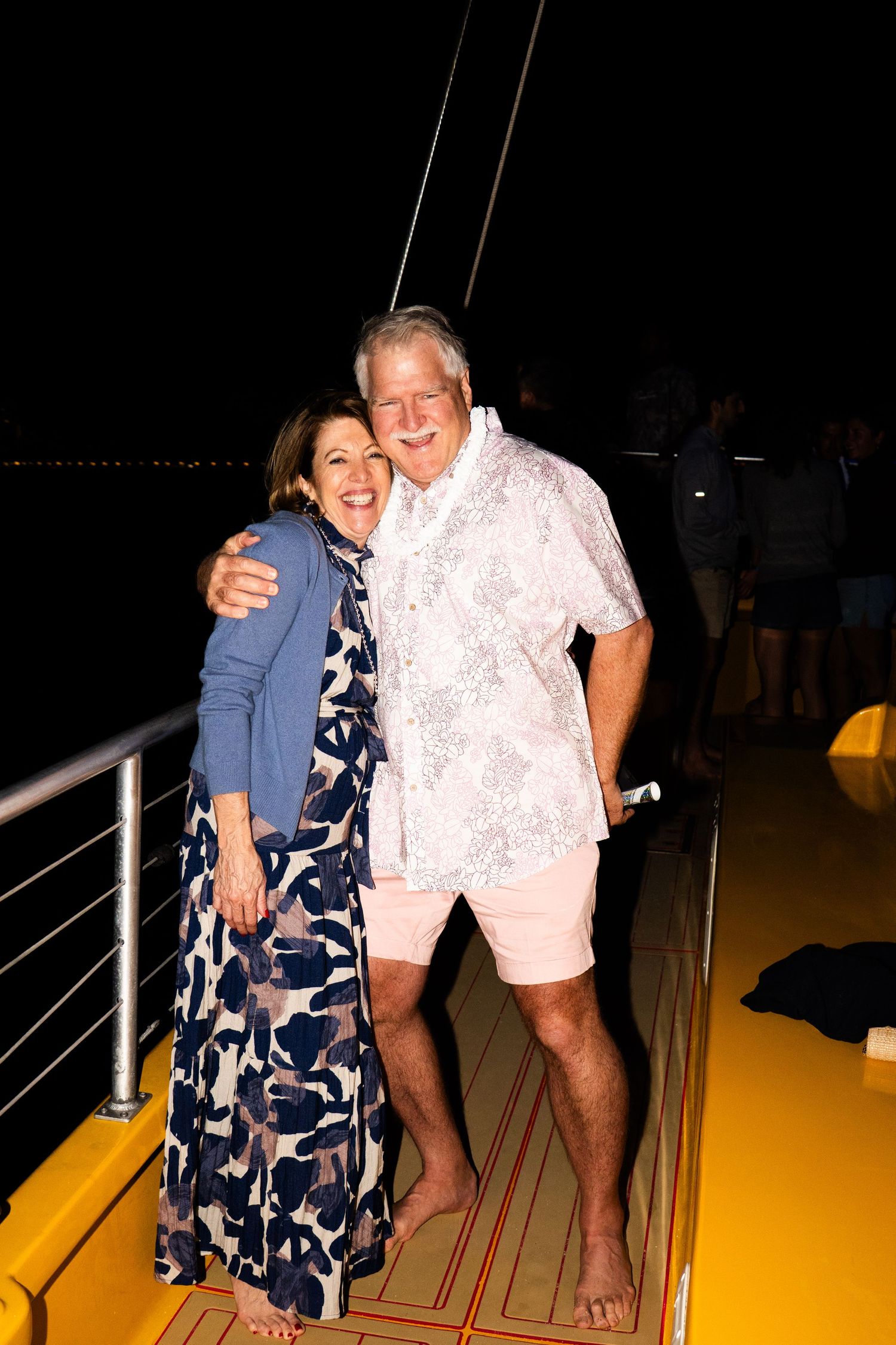 Happy older man and young woman smiling together at the beach, wearing floral outfits with ocean backdrop.