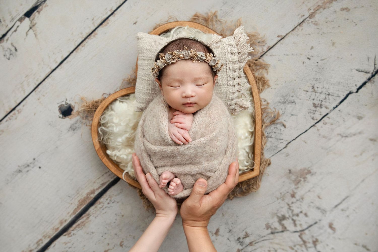 Sleeping newborn baby girl in pink floral romper and headband posed on beige backdrop.