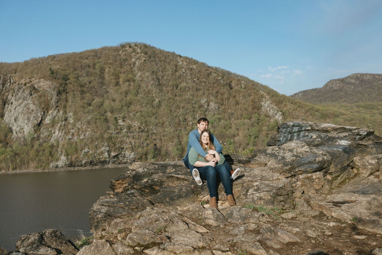 Couple standing on a rustic wooden arched bridge surrounded by bare winter trees in a forest setting.