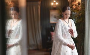 Woman in elegant white embroidered saree with beaded necklace, reflected in mirror, traditional Indian bridal attire.