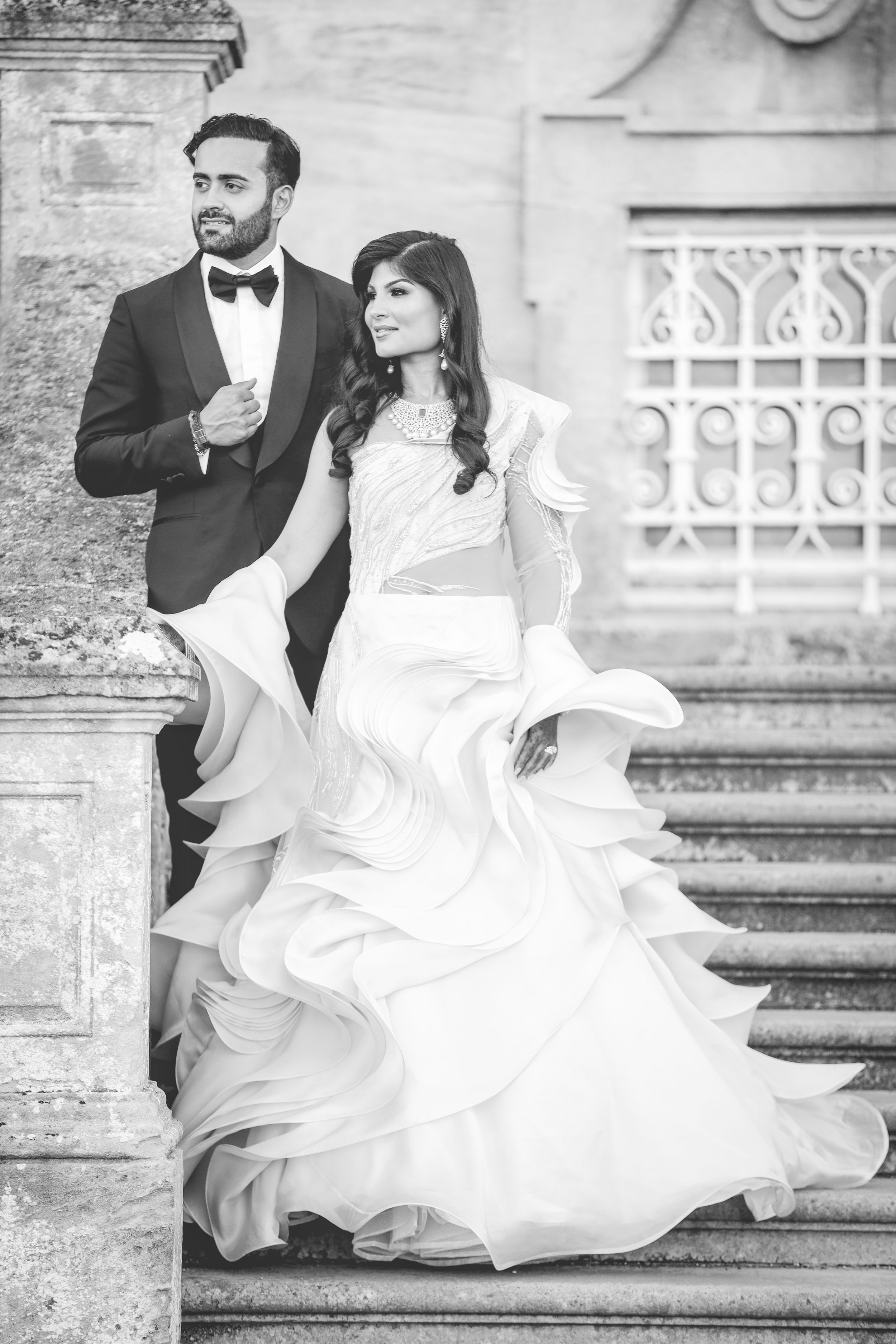 Black and white photo of an elegant couple in wedding attire posing on grand stone steps.