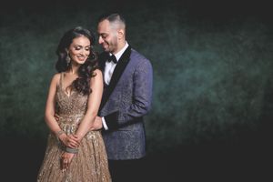Elegant couple in formal attire posing together, man in blue floral tuxedo and woman in gold beaded gown.
