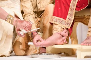 Close-up of hands during an Indian wedding ceremony ritual with henna, gold bangles, and traditional attire.