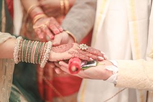 Close-up of Indian bride and groom exchanging rings, bride adorned with mehndi, bangles, and gold jewelry during wedding ceremony.