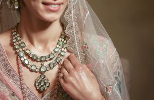 Bride wearing elegant kundan polki necklace with pink embroidered lehenga and sheer dupatta for Indian wedding.