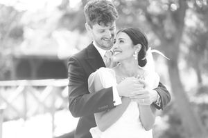 Black and white wedding photo of a smiling bride and groom embracing outdoors on their special day.