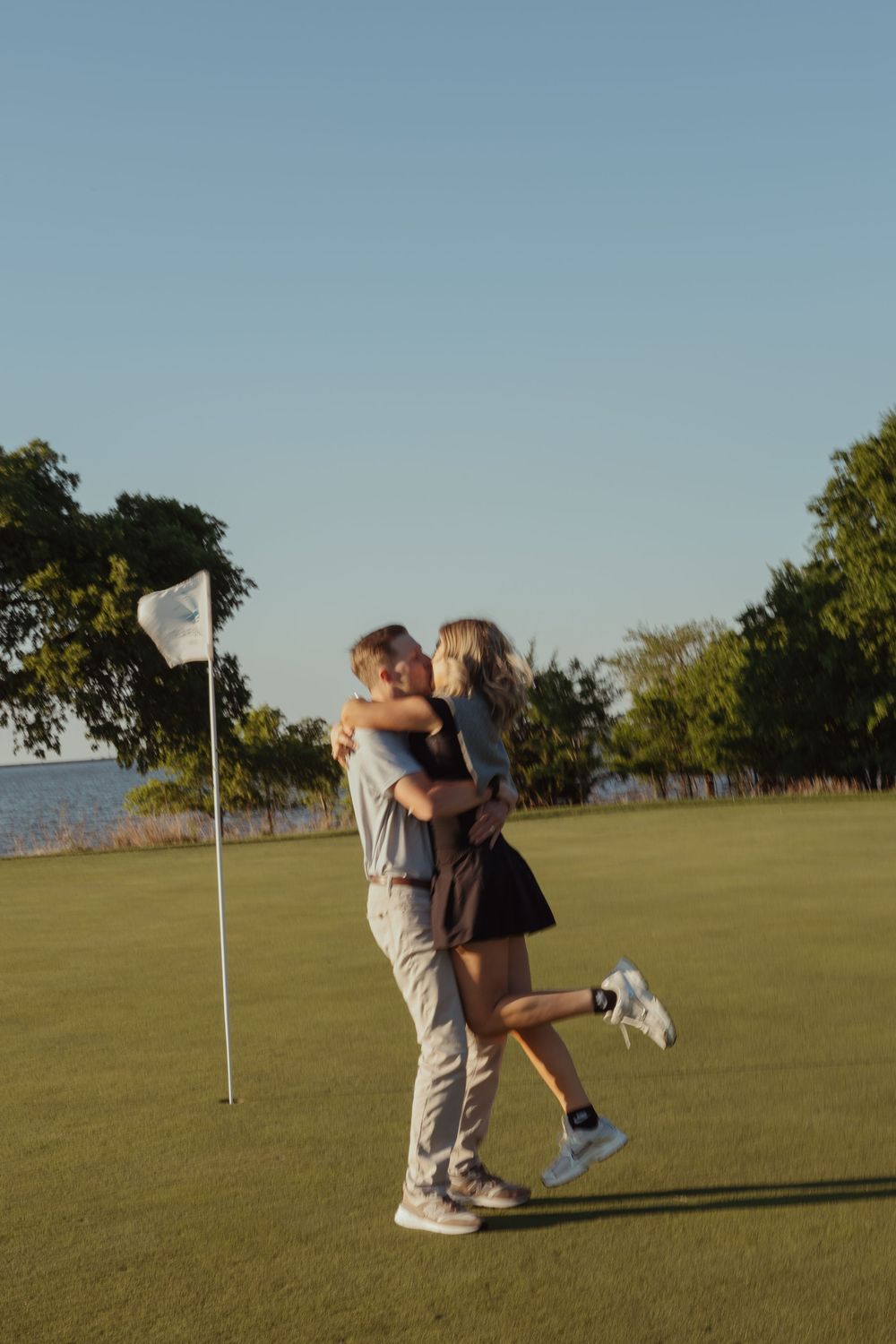 Couple embracing and hugging on a golf course green near a flag pin at sunset.
