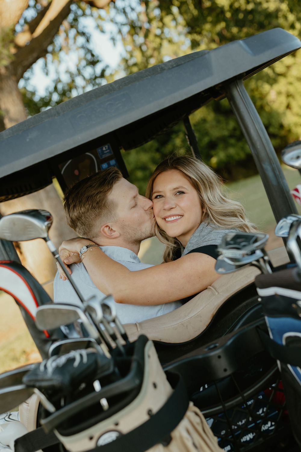 Couple sharing a romantic kiss in a golf cart on a sunny golf course.