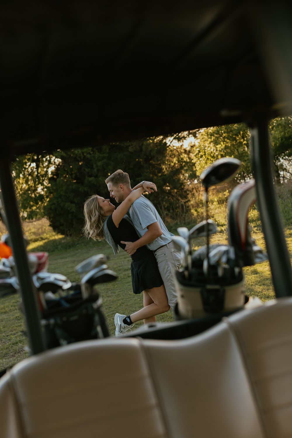 Romantic couple embracing and kissing on a golf course, viewed through the seats of a golf cart.