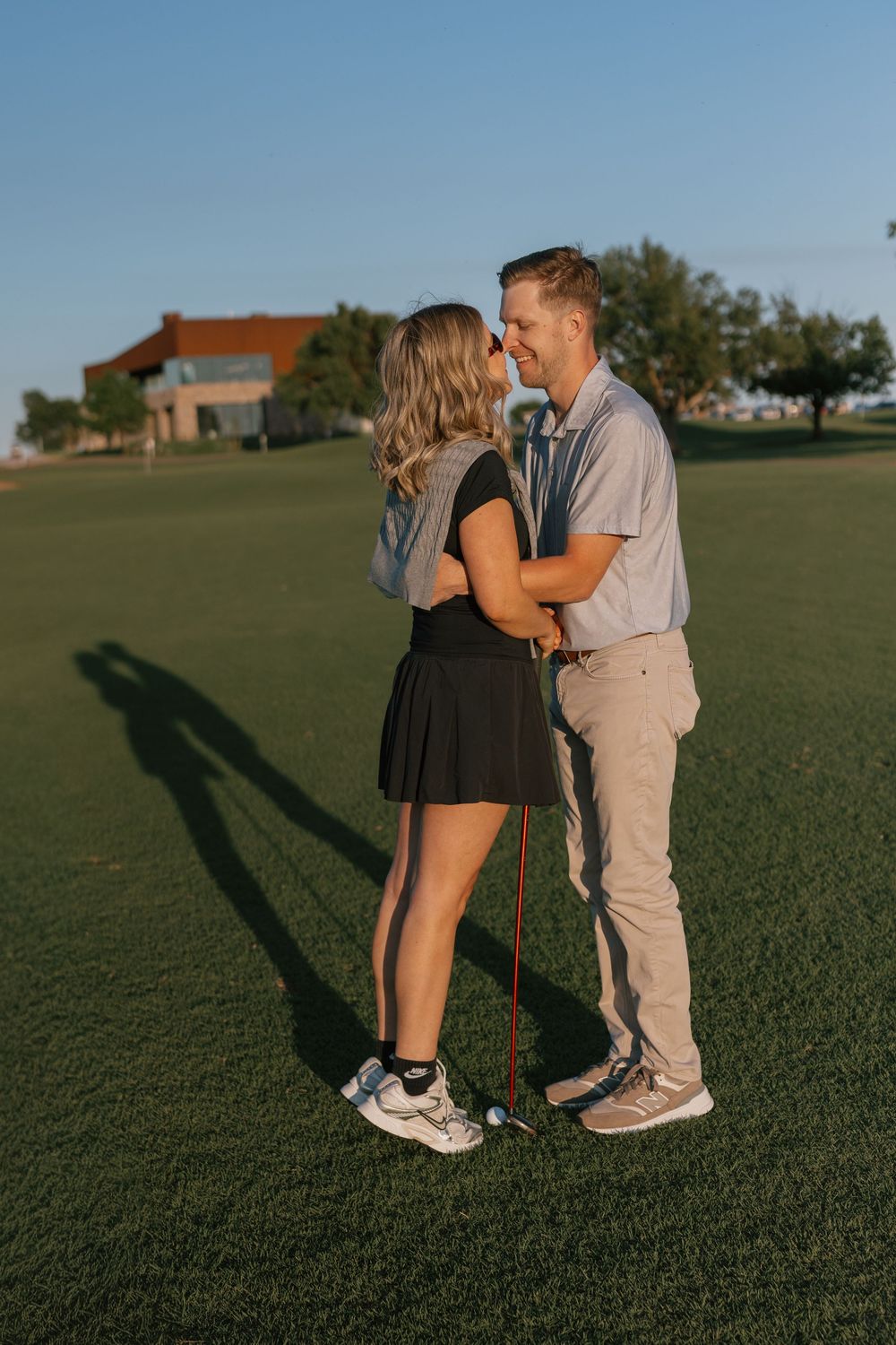 Romantic couple embracing on a sunny golf course, smiling at each other while holding a golf club together.