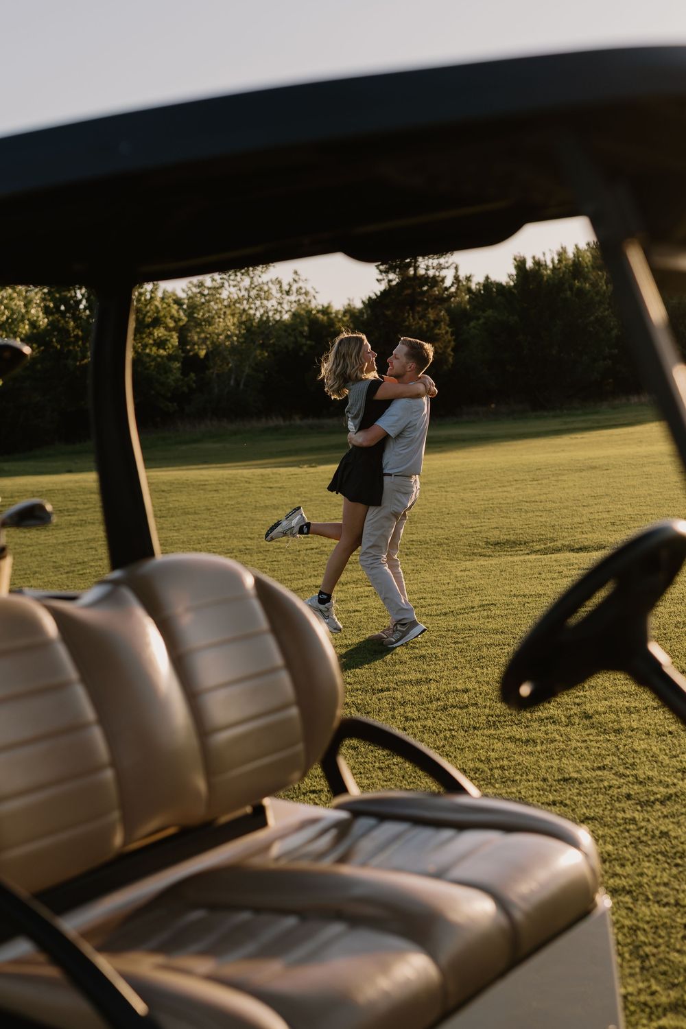 Romantic couple hugging on a golf course green viewed from behind a golf cart at sunset.