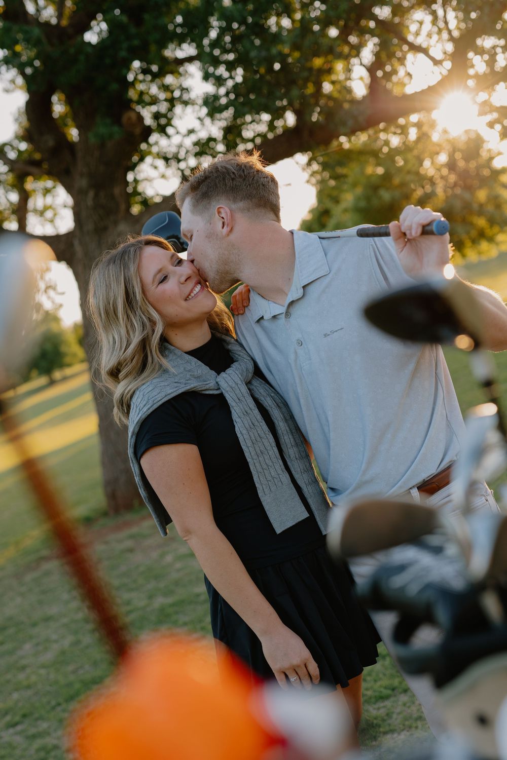 Couple sharing a tender kiss on a golf course at golden hour sunset.
