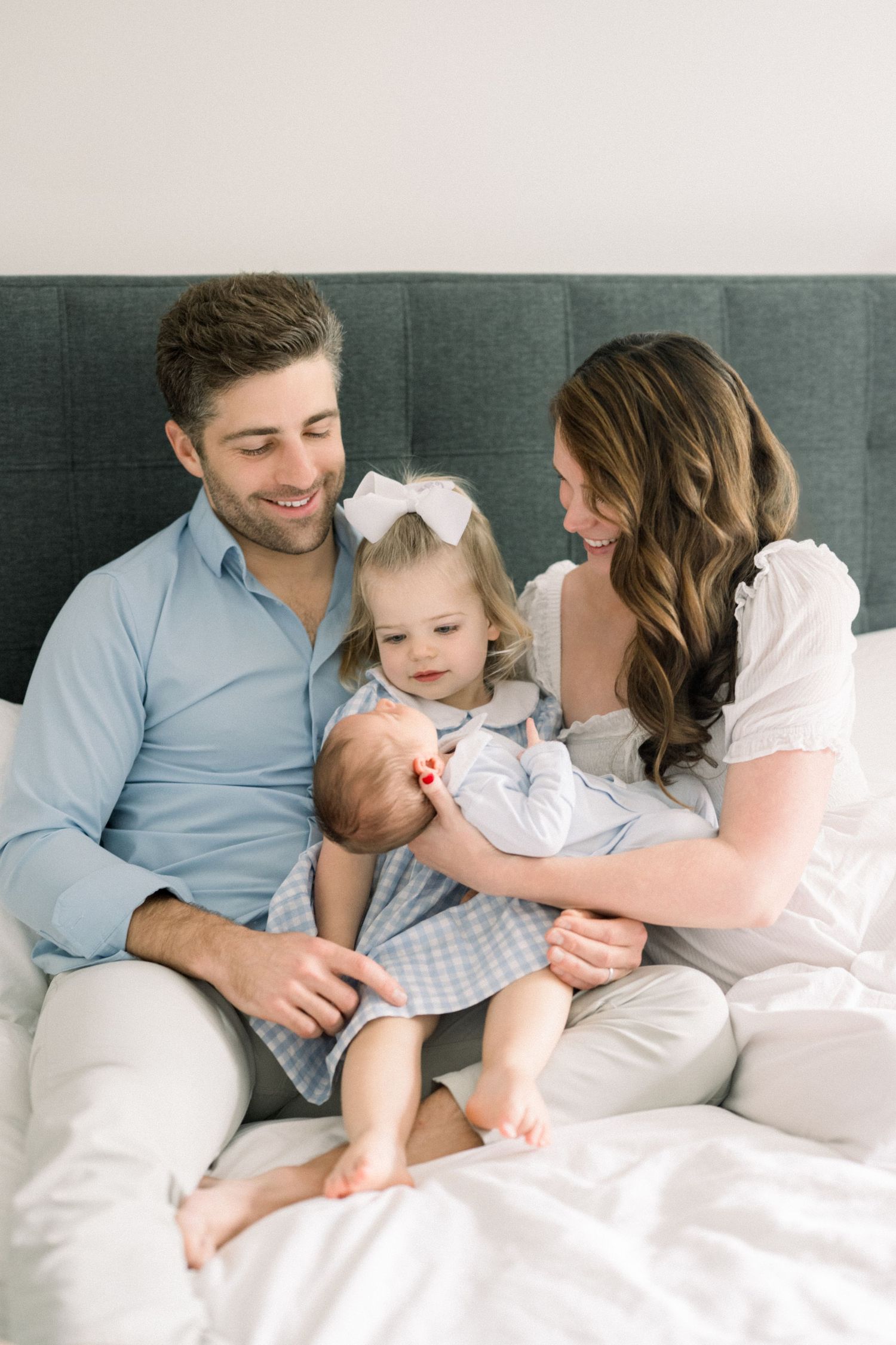 family sitting on bed smiling at baby at an in home newborn session in washington dc