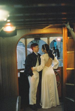 Couple in wedding attire sharing a romantic moment aboard a vintage wooden boat interior with warm lighting.