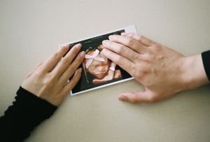 Two hands touching a 3D ultrasound photo on a table, sharing a tender moment with their unborn baby.