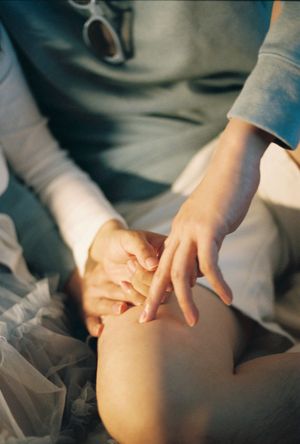 Close-up of two people gently holding hands on a knee, wearing casual clothing in soft natural light.