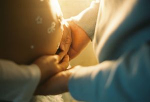 Close-up of medical professionals holding a newborn baby's hand during delivery in a hospital setting.