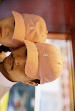 Man wearing a pink baseball cap reflected in a mirror, showing dual angles of the blush-toned hat.