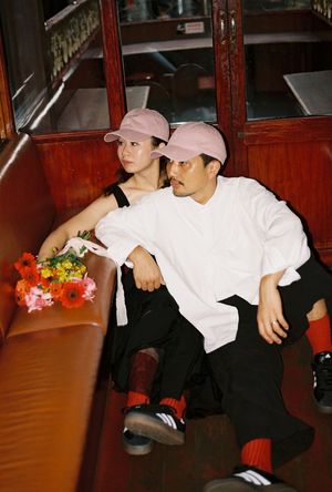 Couple wearing matching pink caps sitting together on a vintage tram seat with colorful flowers nearby.
