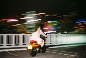Blurred motion shot of a motorcyclist riding at night with colorful light streaks on a bridge.