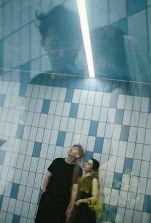 A couple stands beneath a fluorescent light by tiled walls, with a ghostly reflection overhead in a dreamy double exposure.