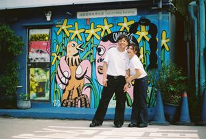 Couple posing in front of colorful street art mural on blue wall at YuYu Bike Parking in Taiwan.