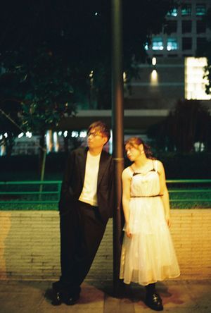 Couple posing at night by a lamppost, man in black suit and woman in white dress, urban background.
