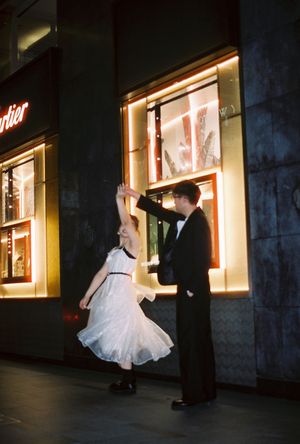 Couple dancing elegantly outside a Cartier store at night, man in tuxedo spinning woman in white dress.