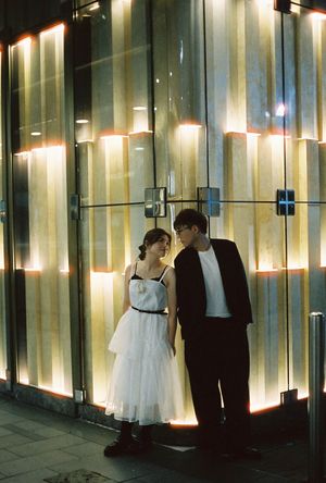 A couple in formal attire shares a tender moment outside a glowing illuminated wall at night.