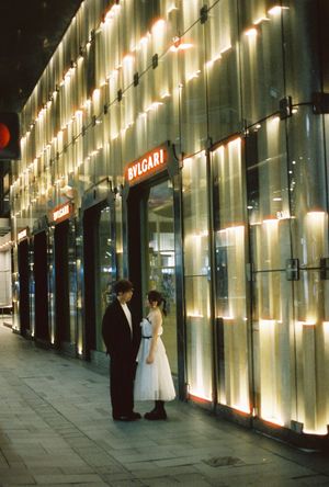 Couple in formal attire standing outside illuminated Bvlgari luxury store at night.